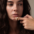 A woman with long dark hair poses with her finger near her lips, showcasing the elegant Cosmic Moonstone Ring—an eye-catching boho jewelry statement.