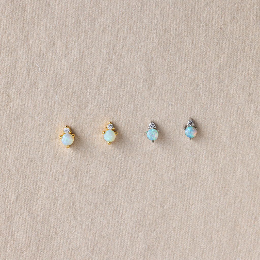Four Raindrop Peridot Studs—two in gold, two in silver settings—rest on a beige textured background. Elegant as birthstone studs or delicate earrings for any occasion.