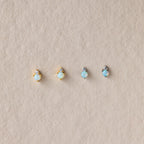 Four Raindrop Peridot Studs—two in gold, two in silver settings—rest on a beige textured background. Elegant as birthstone studs or delicate earrings for any occasion.