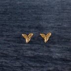 Two Shark Tooth Flatback Studs in 18K Gold rest on a dark textured fabric background—an ideal summer jewelry pick or beach-day accessory.