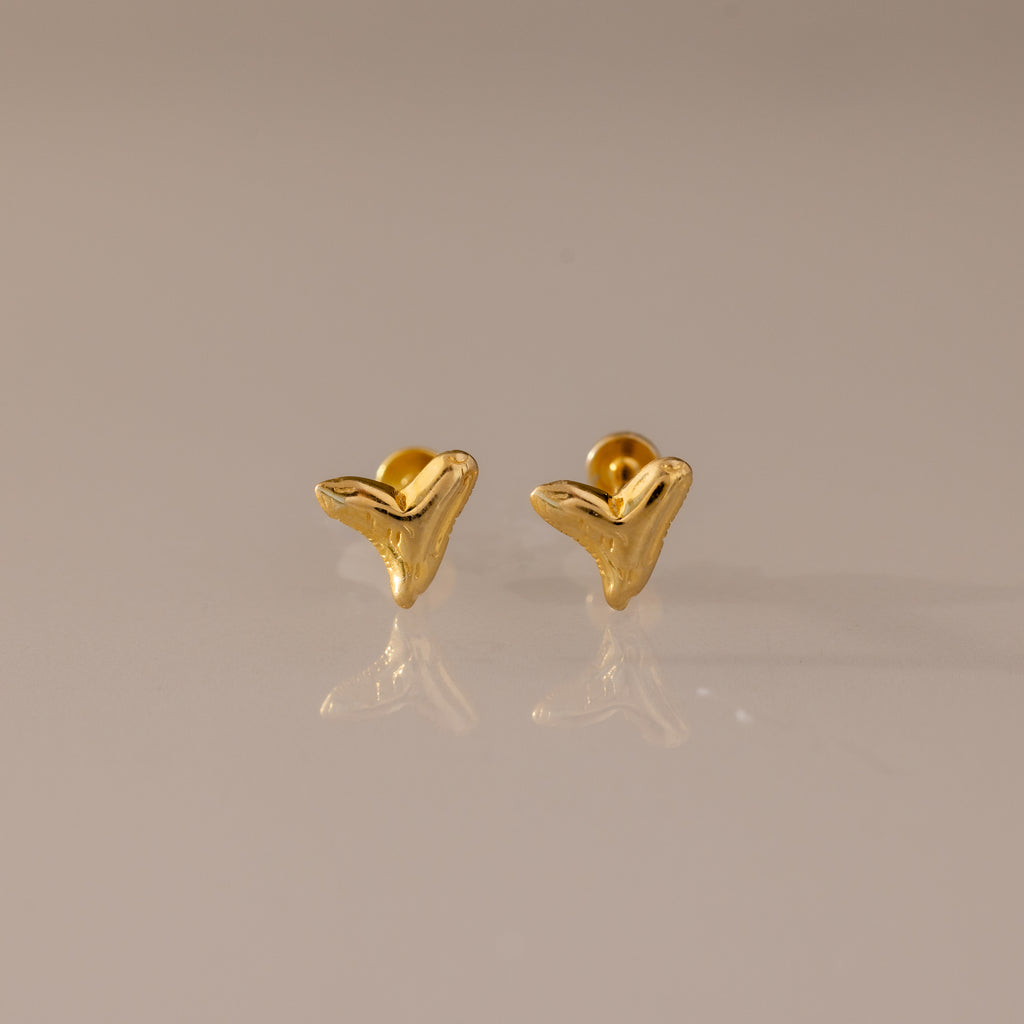 Shark Tooth Flatback Studs in 18K Gold are small, abstract chevron-shaped earrings—perfect as a summer jewelry choice, shown here on a neutral reflective surface.