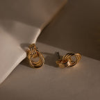Micro Triple Knot Earrings in 18K Gold rest on a neutral surface, softly illuminated to highlight their effortless quiet luxury.