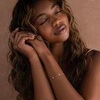 A woman with long wavy hair and closed eyes wears light clothing and the Heart Station Bracelet in Sterling Silver, adding a delicate, romantic touch to her serene look.