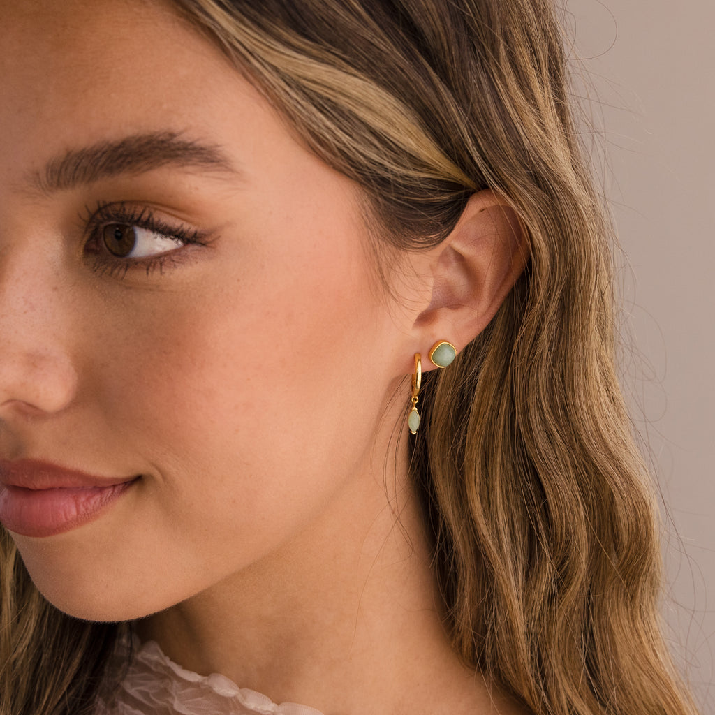 Woman with wavy hair wearing Jade Marquise Huggies, gold and green botanical earrings, looking slightly to the side.