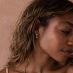 Close-up of a woman with wavy hair wearing Heart Pearl Drop Earrings in Silver against a neutral background.