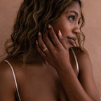 A woman with wavy hair gently touches her face, wearing the Pave Double Knot Ring in soft natural lighting.