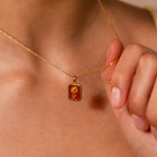 A person holds the Emerald Birth Flower Charm Necklace close to their chest, highlighting its elegant and meaningful design.