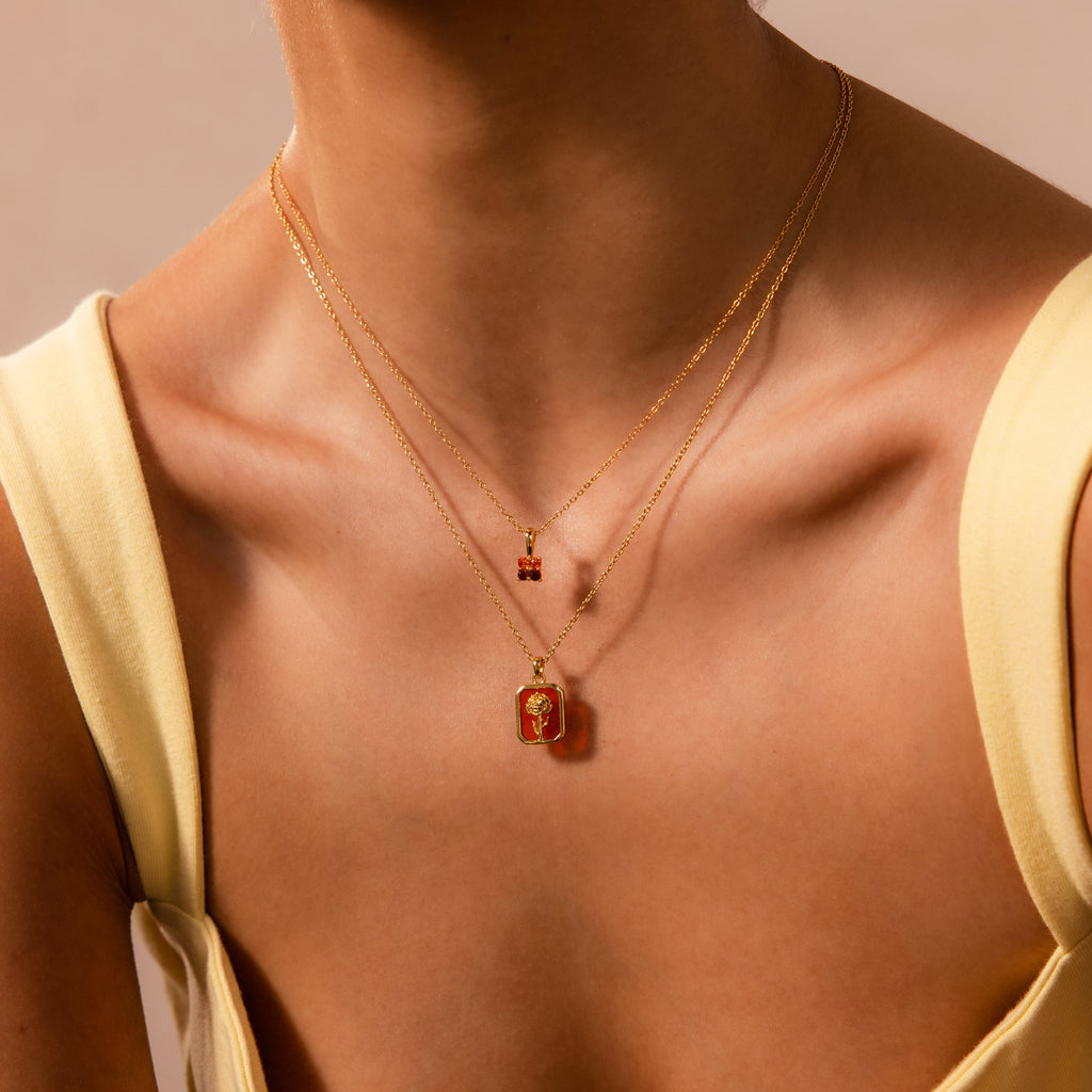 Woman wearing the Opal Birth Flower Charm Necklace, featuring layered gold chains with opal and floral charms, styled with a pale yellow sleeveless top—please provide the product description for SEO keyword extraction.