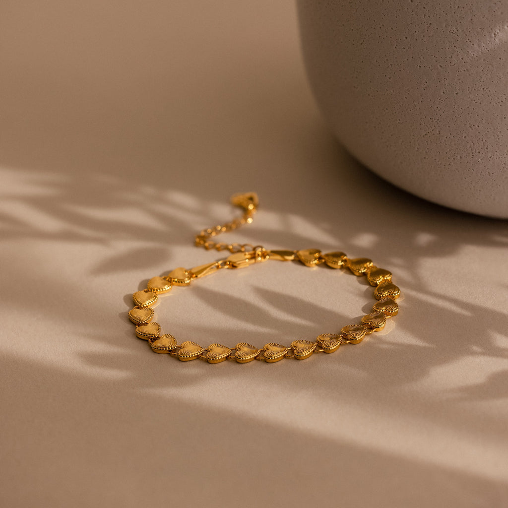 The Ribbed Heart Link Bracelet is laid flat on a matte beige surface, with soft, natural light casting delicate shadows