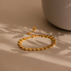 The bracelet laid flat on a neutral beige surface next to a ceramic vase, with soft shadows cast across it.