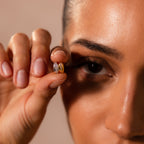 A woman holds two Pave Dome Charms near her eye, highlighting their detailed gold and silver design—ideal for stacking or pairing with other delicate jewelry.