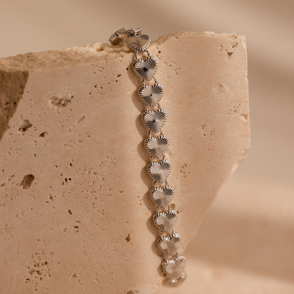 A vertical close-up of the Ribbed Heart Link Bracelet in White Gold draped over a textured stone surface.