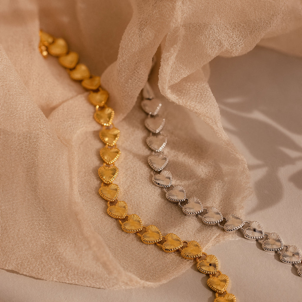  Two Ribbed Heart Link Bracelets, one in gold and one in white gold, displayed side by side on beige fabric.