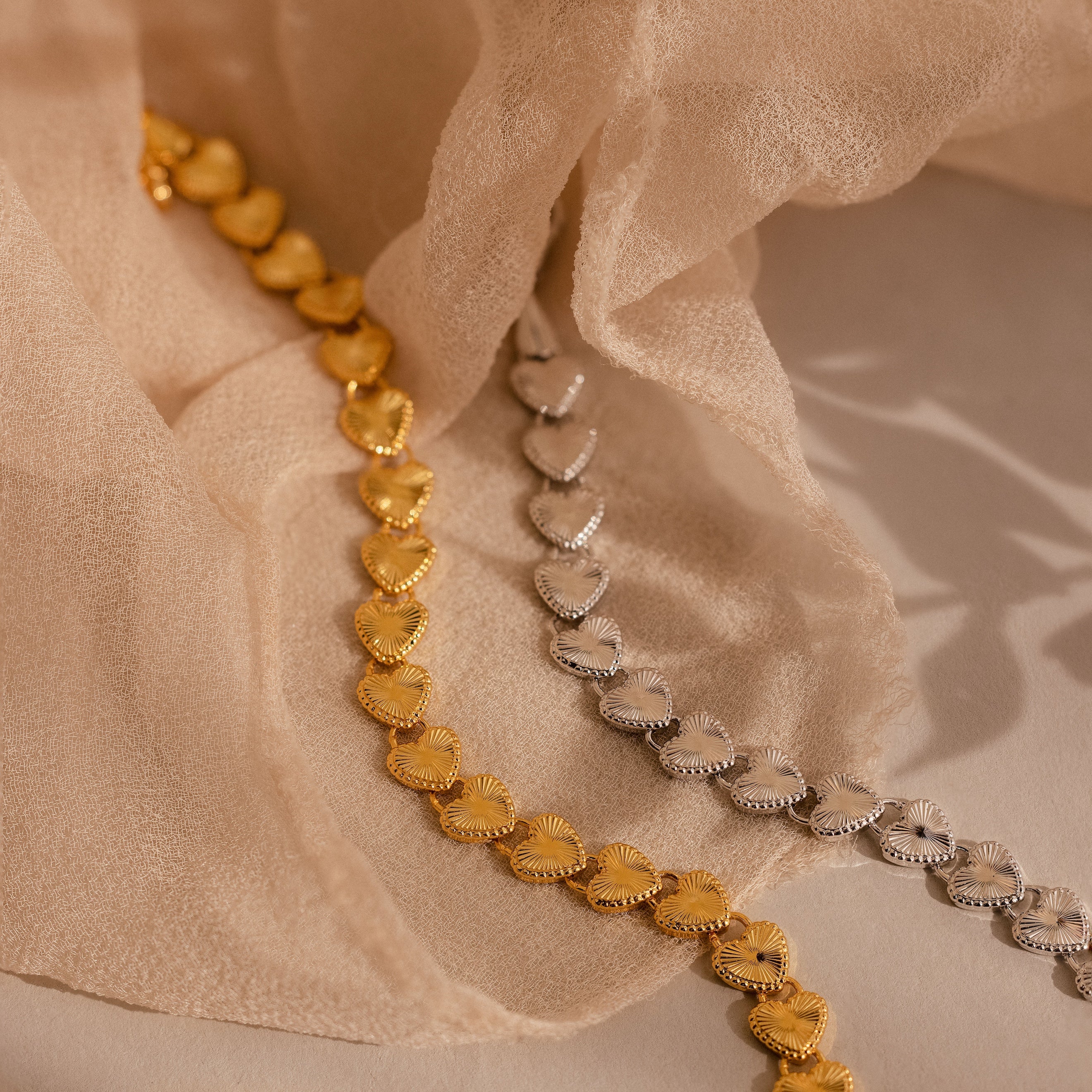  Two Ribbed Heart Link Bracelets, one in gold and one in white gold, displayed side by side on beige fabric.