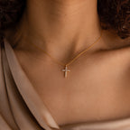 A woman wearing the Pave Cross Necklace in 18K Gold, featuring a jeweled cross pendant on a gold chain, paired with a beige satin top.