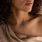 Woman with curly hair wears a Pave Cross Necklace in Silver and a beige off-shoulder top, shown from the shoulders up to highlight her elegant jewelry style.