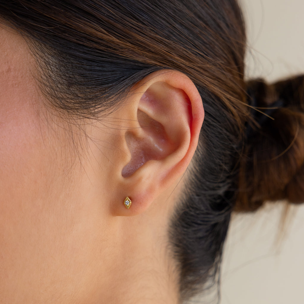 Close-up of a woman’s ear adorned with Ericka Diamond Studs; her hair is tied back in a bun, highlighting the delicate gold earrings.