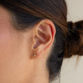 Close-up of a woman’s ear adorned with Ericka Diamond Studs; her hair is tied back in a bun, highlighting the delicate gold earrings.