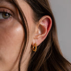 Close-up of a woman's ear wearing Beaded Hoops in 18K Gold with textured details, her hair partially covering her face.