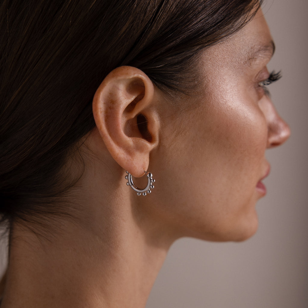 Woman with straight brown hair wears Beaded Hoops in Sterling Silver, adding a textured glow to her ear.