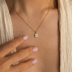 A person wearing the North Star Gemstone Necklace in 18K Gold touches their chest with manicured, light pink nails.