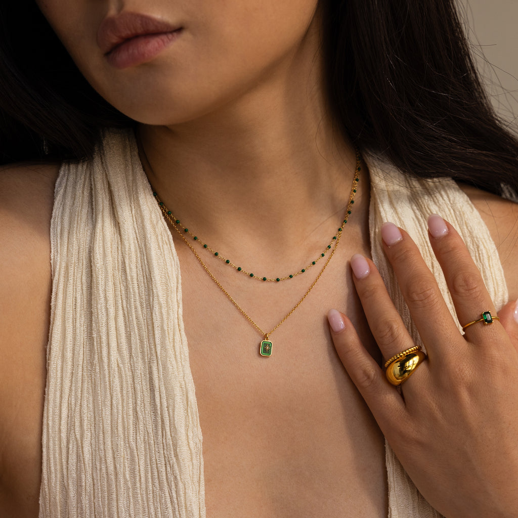 Woman wearing two gold necklaces—including the North Star Gemstone Necklace in 18K Gold—paired with a gold ring and a cream textured sleeveless top.