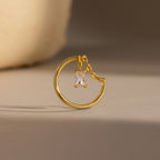 The Birthstone Drop Chain Ring features a gold band with an emerald-cut stone dangling delicately on a chain, showcased against a neutral background.