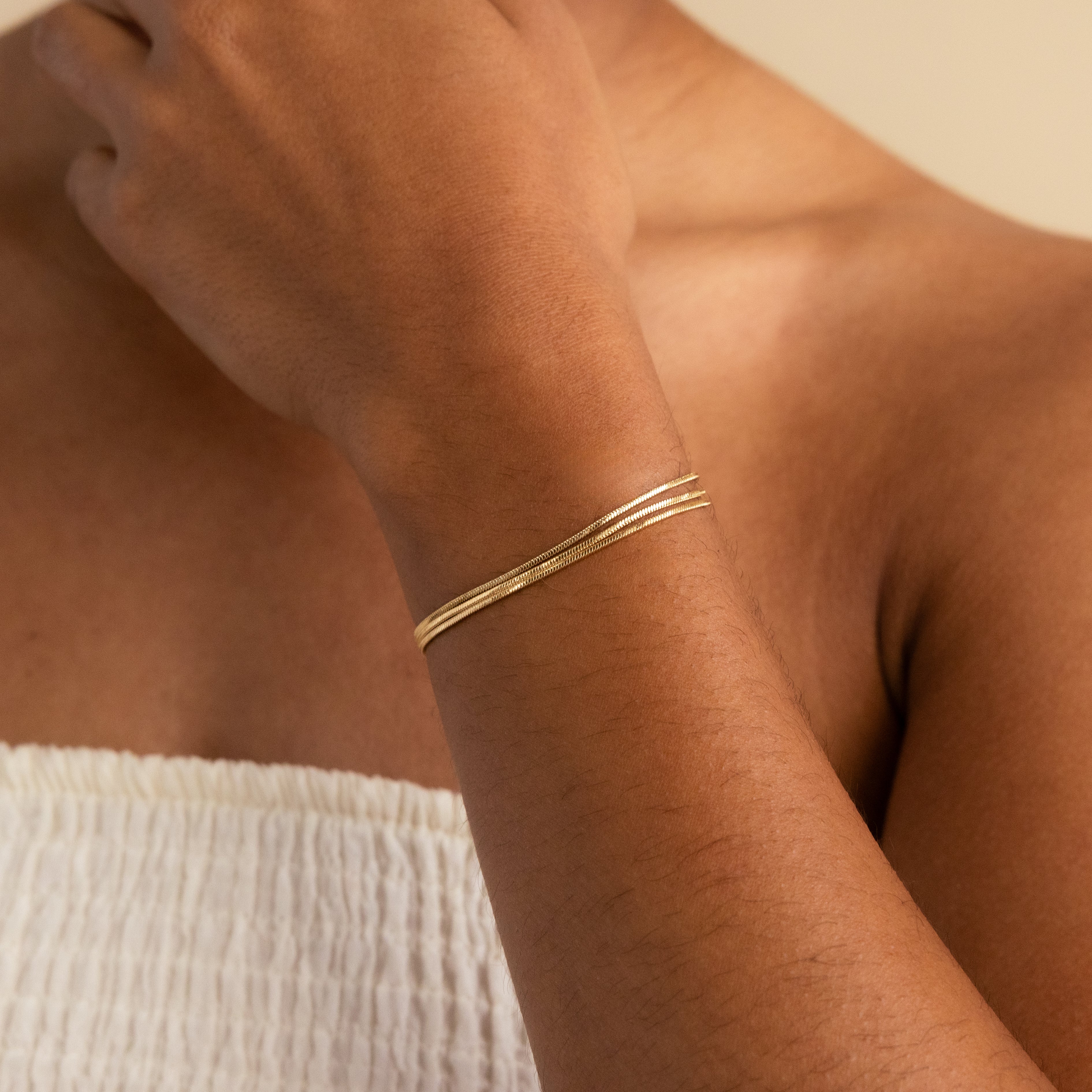 Someone with a minimal jewelry style wears the Triple Snake Chain Bracelet paired with a white, textured sleeveless top.
