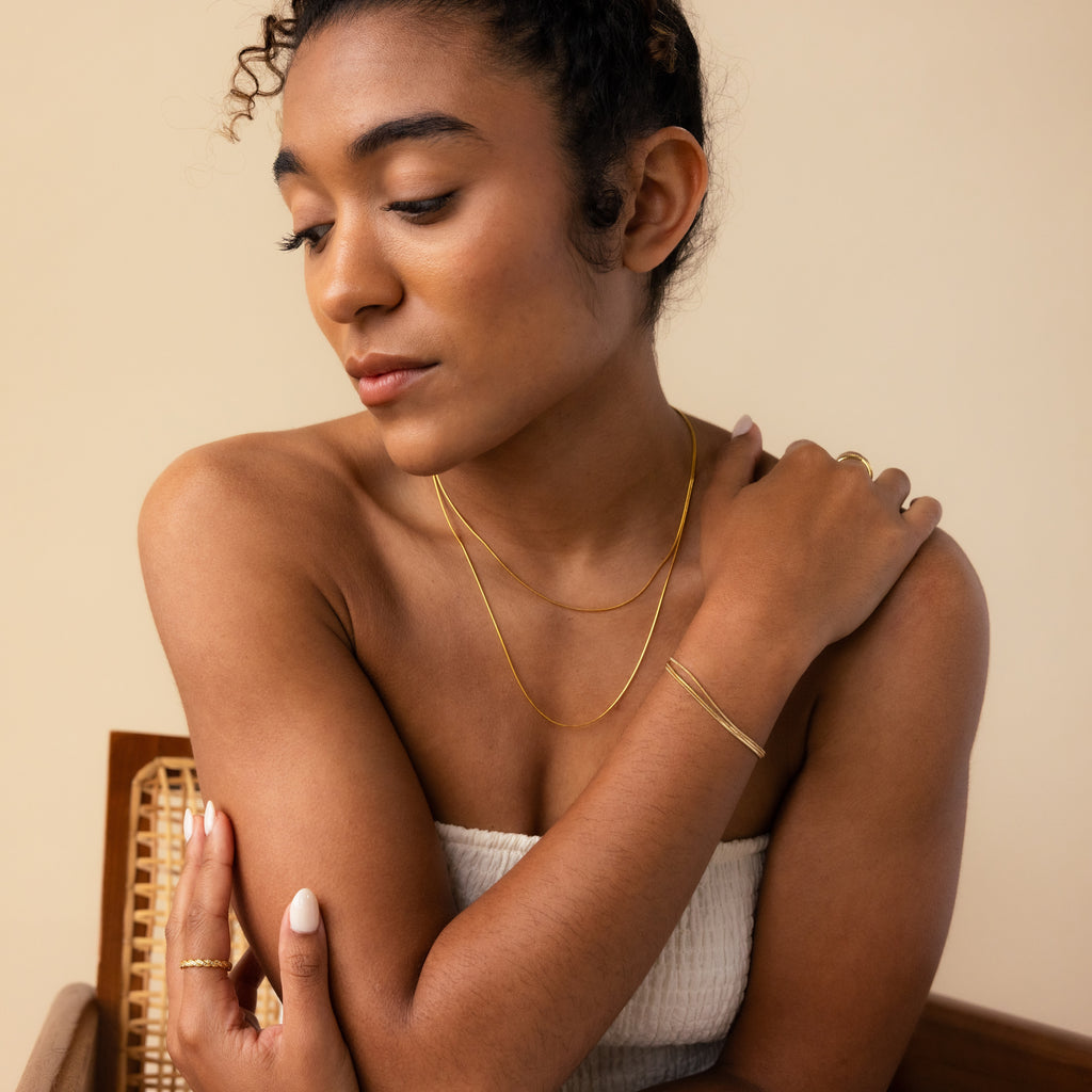 A woman in a white top poses gracefully, wearing the Triple Snake Chain Bracelet in White Gold as minimal jewelry and gazing downward with a serene expression.