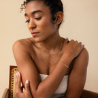 A woman in a white top poses gracefully, wearing the Triple Snake Chain Bracelet in White Gold as minimal jewelry and gazing downward with a serene expression.