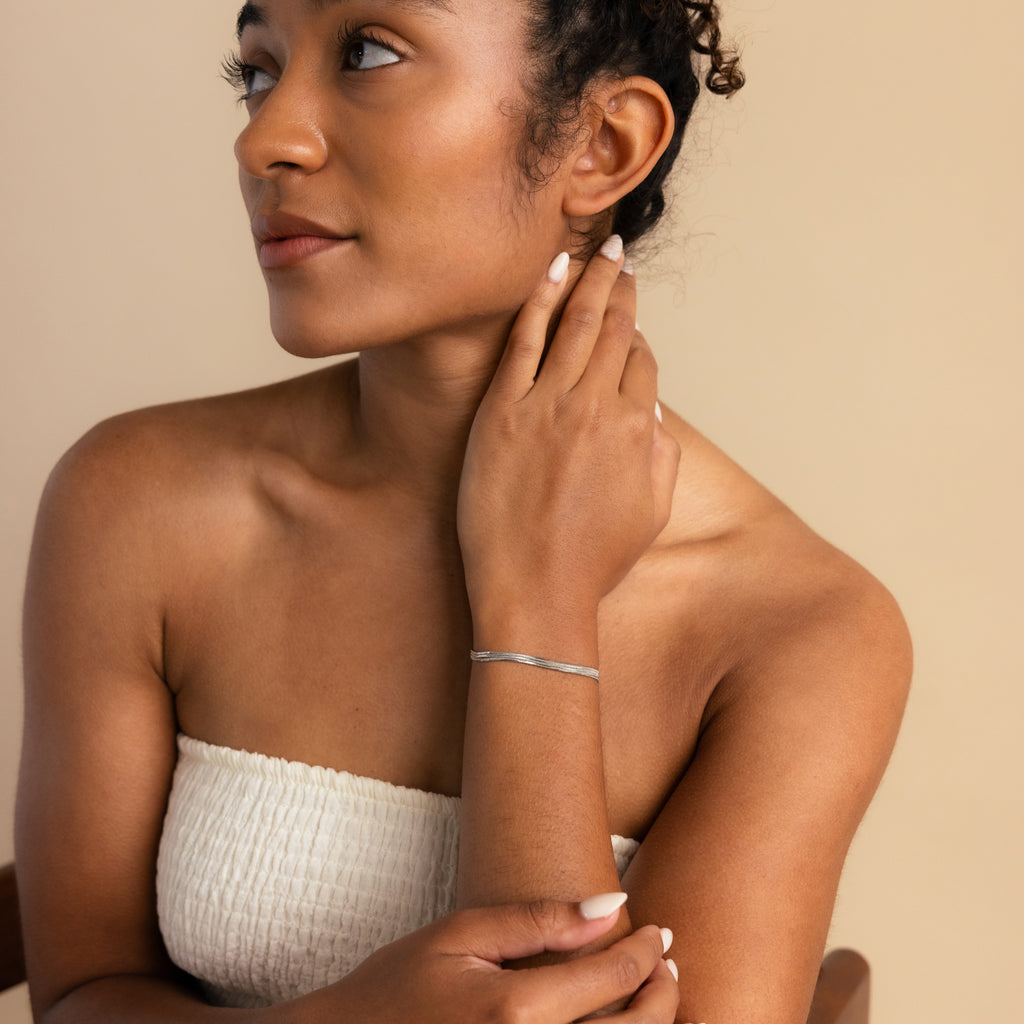 Woman in a white strapless top touches her neck, wearing minimal jewelry including the Triple Snake Chain Bracelet in White Gold, and looks to the side.