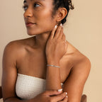 Woman in a white strapless top touches her neck, wearing minimal jewelry including the Triple Snake Chain Bracelet in White Gold, and looks to the side.