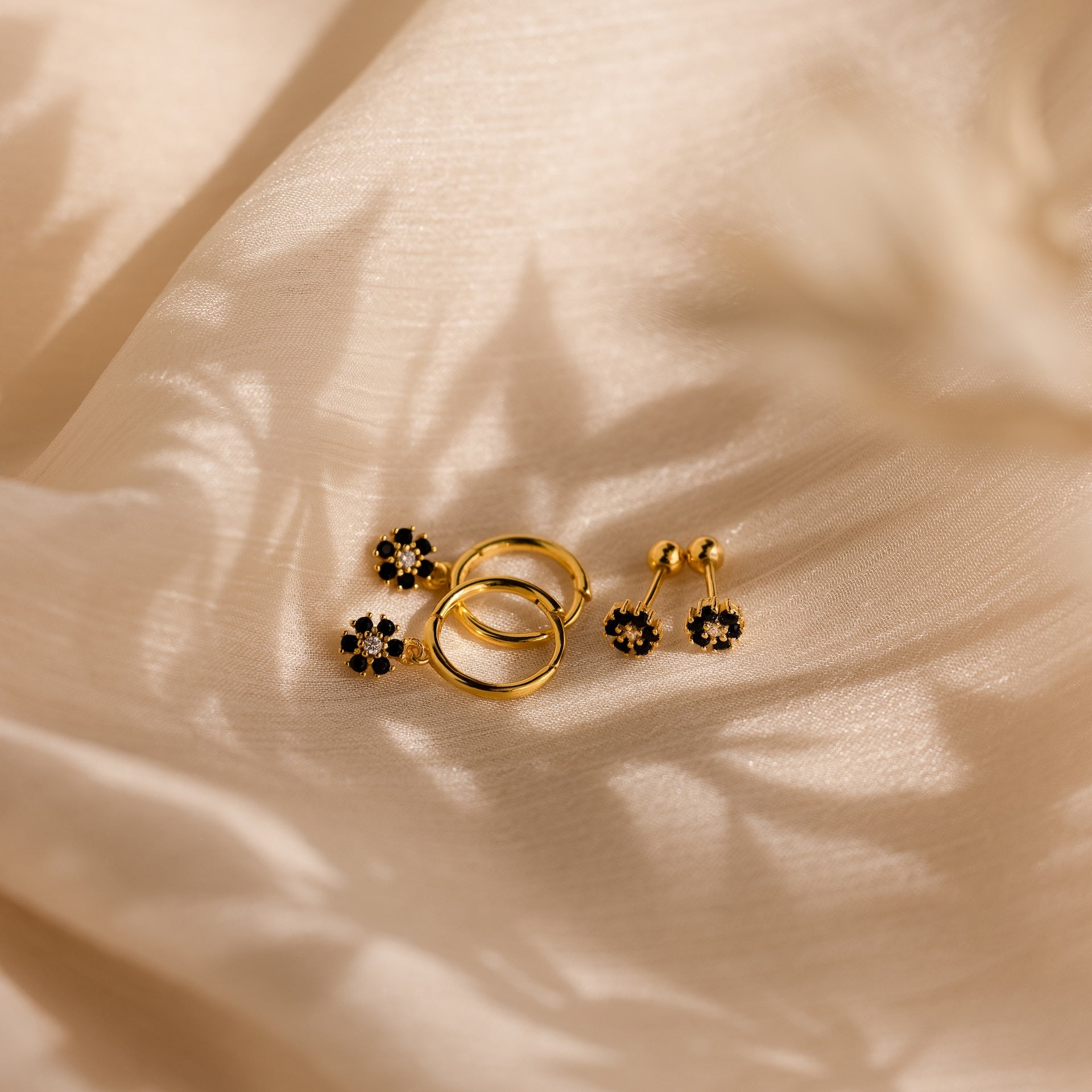Onyx Flower Studs in 18K Gold with black onyx accents are displayed on cream-colored textured fabric, casting soft shadows.