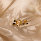 Onyx Flower Studs and gold rings lie on beige silky fabric, illuminated by gentle light and soft shadows.