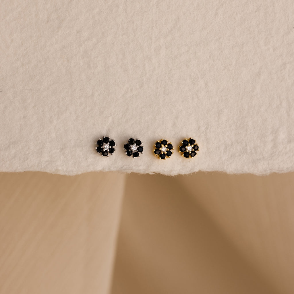 Two silver and two gold small floral stud earrings are arranged on a textured cream surface—style them with Onyx Flower Studs in Silver for a chic, curated ear look.