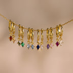 Nine Birthstone Drop Huggies featuring colorful gemstone charms on thin gold chains, perfect for personalized jewelry. Displayed against a neutral background.