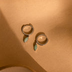 Jade Marquise Huggies in Silver displayed on a sandy beige background under soft light.