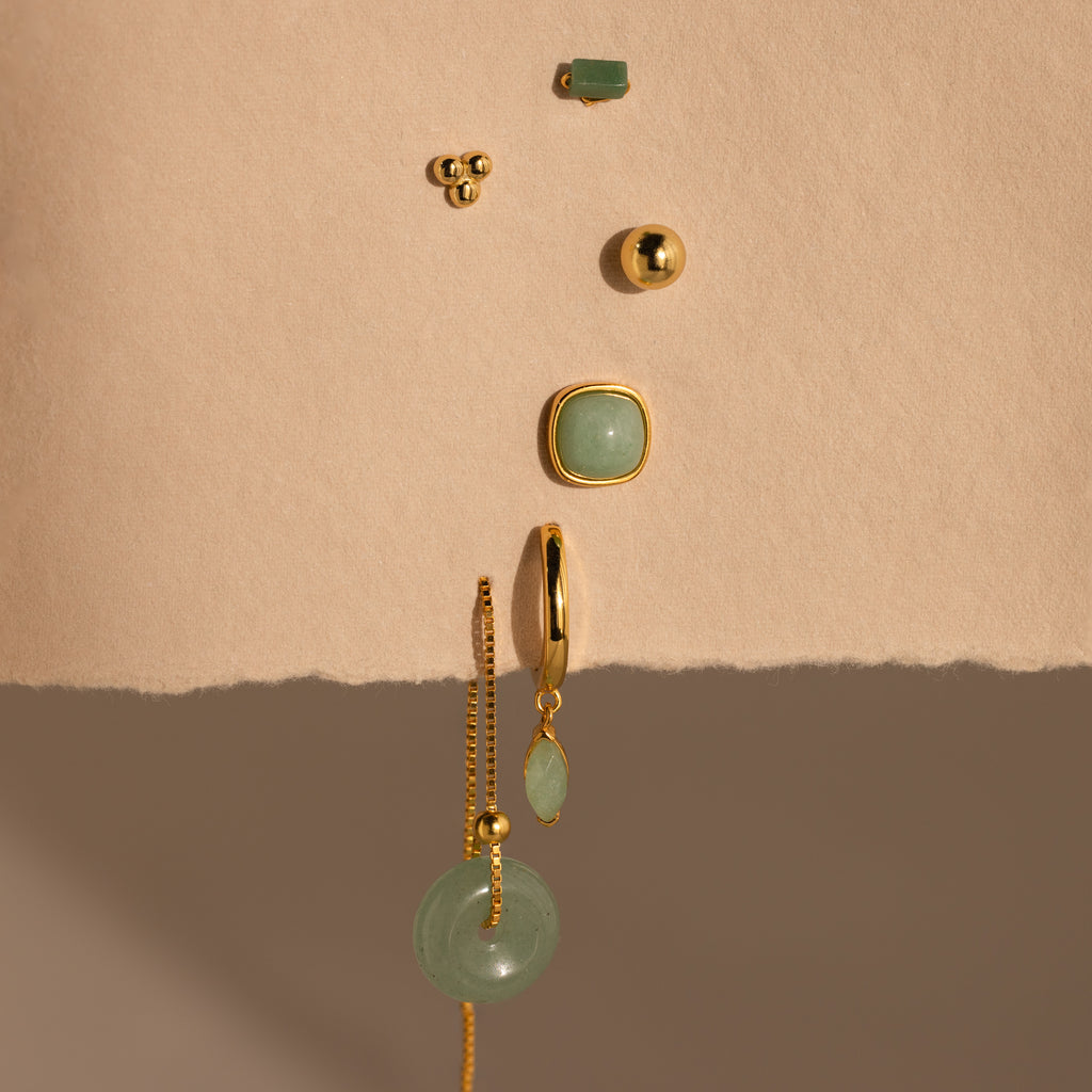 Jade Marquise Huggies, elegant gold and green earrings, displayed vertically on a textured beige background.