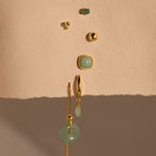 Jade Marquise Huggies, elegant gold and green earrings, displayed vertically on a textured beige background.
