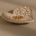 A pair of gold huggie earrings with rhombus-cut aquamarine gemstones resting on a textured ceramic dish.