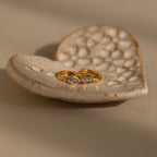 A pair of gold huggie earrings with rhombus-cut aquamarine gemstones resting on a textured ceramic dish.
