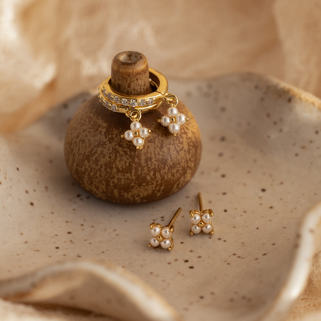 The Pearl Ivy Flower Huggies in 18K Gold are displayed on a ceramic holder, with matching studs arranged on a speckled dish.