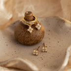 The Pearl Ivy Flower Huggies in 18K Gold are displayed on a ceramic holder, with matching studs arranged on a speckled dish.