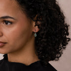 Woman with curly hair wearing Jade Drop Hoops in Silver, shown in profile against a neutral background.