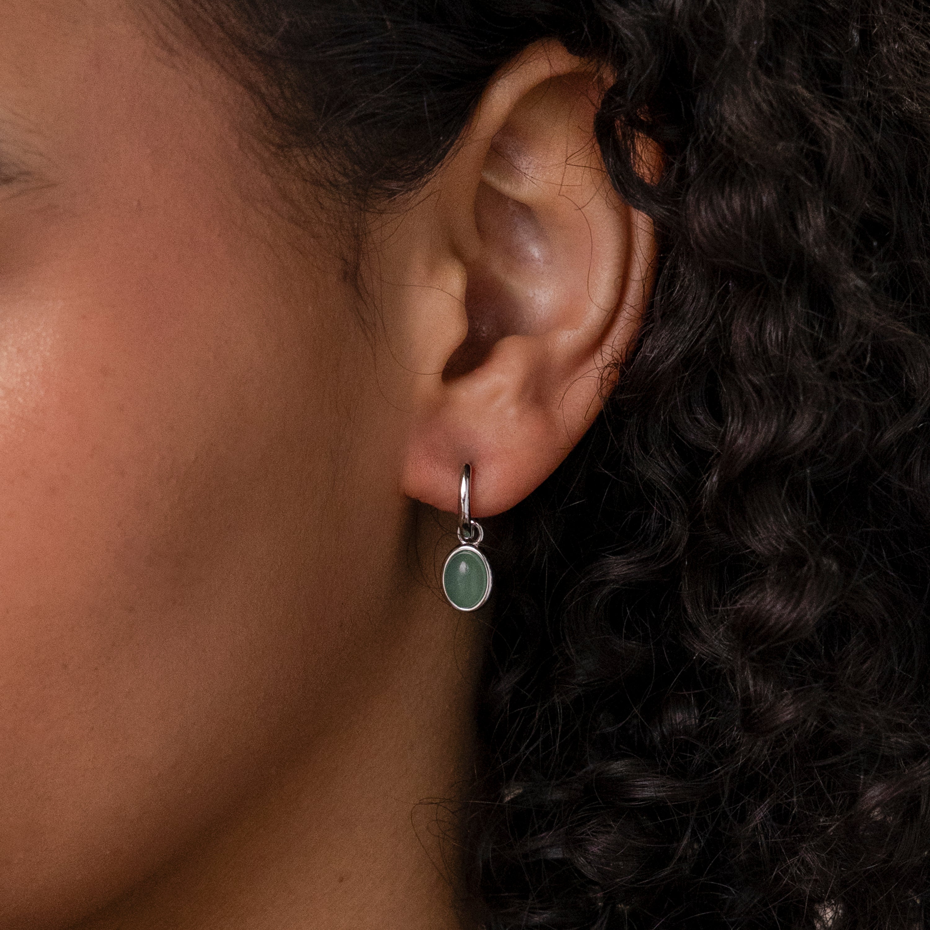 A close-up of an ear wearing the Jade Drop Hoops in Silver, featuring an oval green jade gemstone pendant.