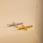 A gold and a silver pave cross charm lay flatly, side by side