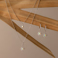 The Opal Star Necklace & Earrings Set in Silver, featuring a necklace and matching earrings, is displayed on dried palm leaves.