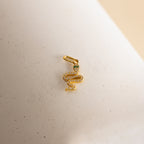 A gold diamond snake charm. The design is a twisting snake with diamond gemstones encased on its body and emerald gemstones for its eyes