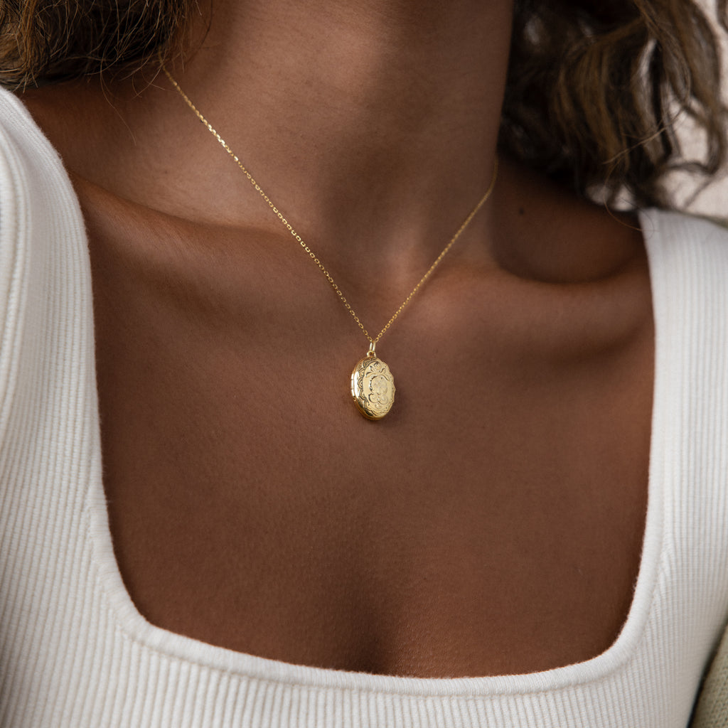 A woman wearing a white square-neck top and the Floral Handwriting Locket Necklace gently resting at her collarbone.