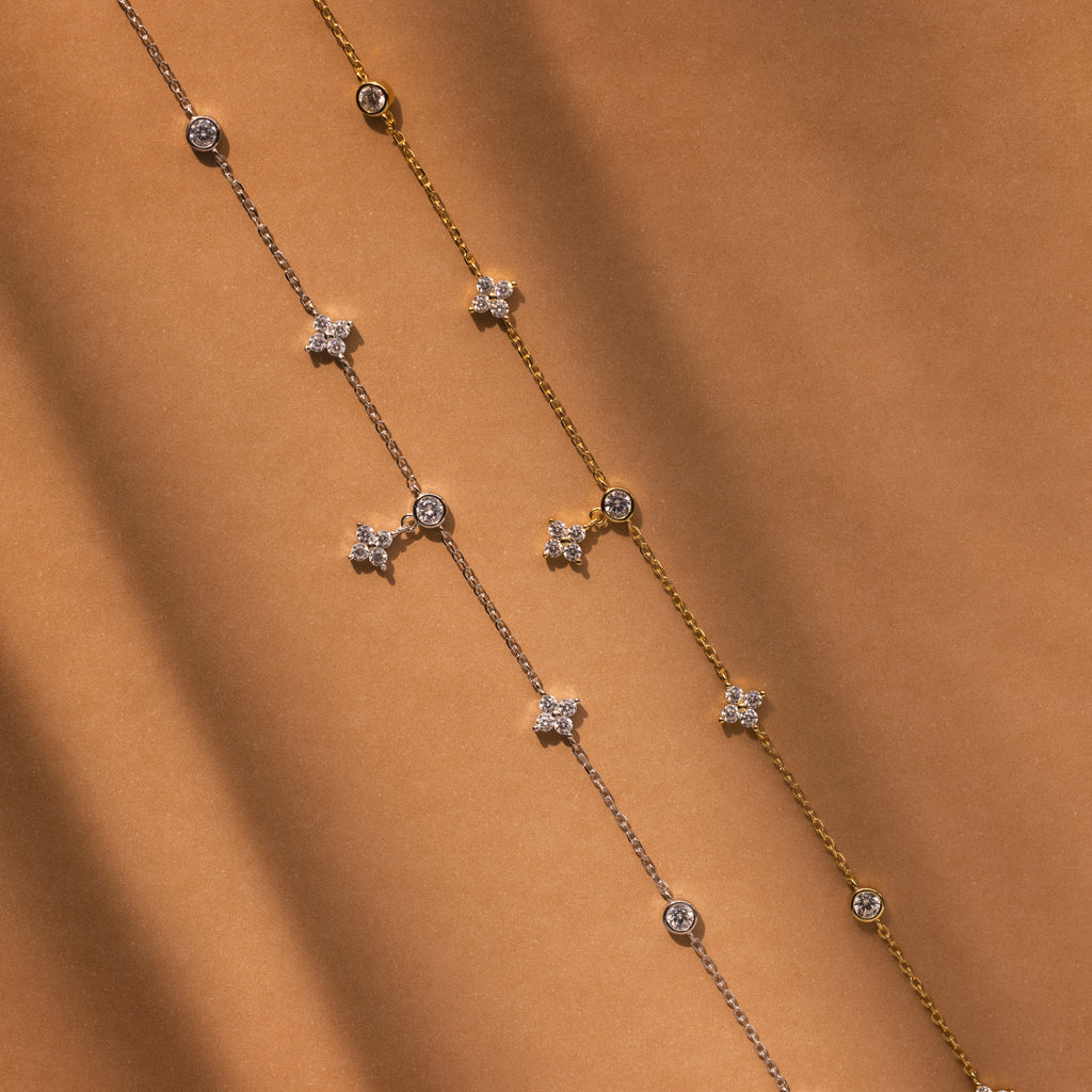 The Ivy Diamond Station Necklace in Silver sparkles with diamond accents, elegantly displayed on a warm brown background.